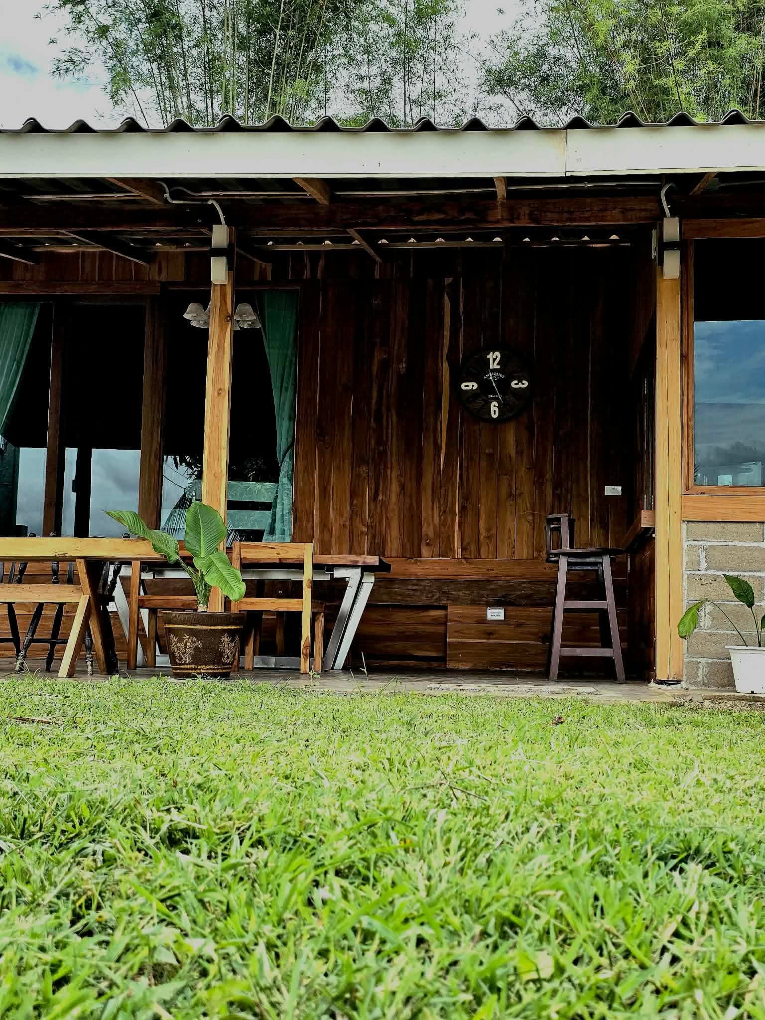A teak porch with a clock, viewed from the grass.